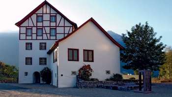 Ensemble de bâtiments historiques des Pfrundbauten avec façade à colombages et décor de montagne au Liechtenstein dans la lumière du soir.