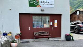 Entrée de la boutique de la ferme Aeulehof avec portail rouge, banc et décoration florale à Triesen, Liechtenstein.