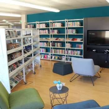 Coin lecture confortable dans la Bibliothèque nationale du Liechtenstein avec fauteuils et mur multimédia entre de hautes étagères de livres