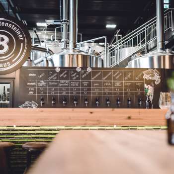 Vue sur la pompe à bière stylée et la zone de brassage avec des cuves en acier inoxydable et un design industriel.
