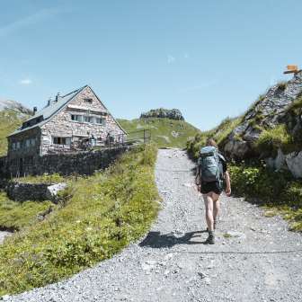 Femme avec sac à dos sur un sentier de montagne juste avant le refuge Pfälzer - décor alpin, itinéraire de randonnée balisé et prairies vertes de haute montagne