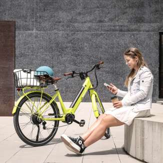 Jeune femme assise avec un café et un smartphone à côté d'un vélo électrique jaune dans le centre urbain de Vaduz