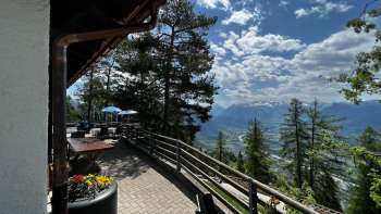 Terrasse ensoleillée de l'auberge de montagne Matu avec vue sur la vallée du Rhin et le paysage montagneux environnant.