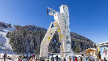 Tour de glace de Malbun sous un ciel bleu, entourée d'arbres enneigés et de skieurs
