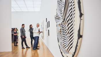 Un groupe de visiteurs dans la salle d'exposition du musée d'art ; au premier plan, une grande œuvre d'art ronde