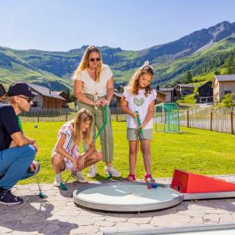 Une famille joue au minigolf ensemble dans le village de montagne ensoleillé de Malbun au Liechtenstein - un plaisir pour petits et grands dans les Alpes.