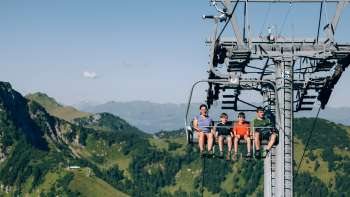 Une famille emprunte le télésiège de Sareis pour traverser un paysage de montagne verdoyant
