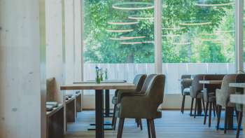 Restaurant lumineux et moderne avec des boiseries, des sièges confortables et de grandes fenêtres avec vue sur la verdure