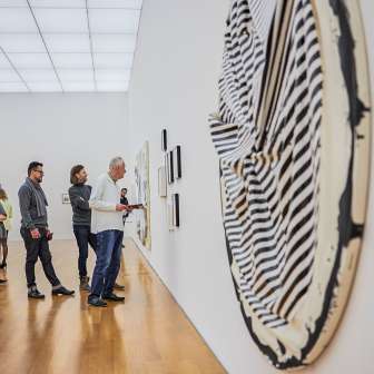 Les visiteurs contemplent des œuvres d'art moderne dans une galerie du Kunstmuseum Liechtenstein à l'architecture lumineuse et au sol en bois.