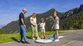  Une famille joue au minigolf ensemble dans les montagnes de Malbun sous un soleil radieux
