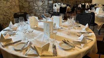 Table ronde élégamment dressée avec nappes, serviettes et menus blancs devant un mur de pierre.