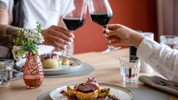 Deux personnes trinquent avec du vin rouge, au premier plan un plat principal soigneusement préparé