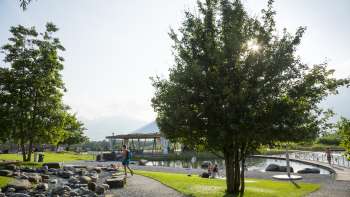 Promenade ensoleillée avec des arbres ombragés et vue sur l'eau dans le parc de loisirs de Grossabünt.
