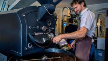 Un homme torréfie des grains de café sur une machine moderne dans un torréfacteur de café.