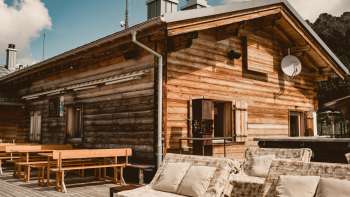 Agréable terrasse ensoleillée avec des bancs en bois et des meubles de salon confortables devant le refuge Sareis à 2.000 mètres d'altitude, sous un soleil radieux et dans un décor de montagne.