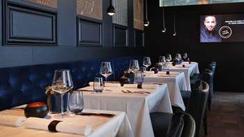 Intérieur élégant de l'Esquire Bar & Bistro à Vaduz avec des tables dressées avec style, une banquette bleu foncé et un éclairage d'ambiance.