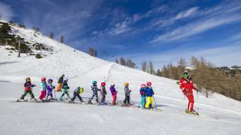 Un moniteur de ski du parc Malbi Malbun motive les enfants sur la pente d'entraînement - un environnement parfait pour les premiers virages dans la neige