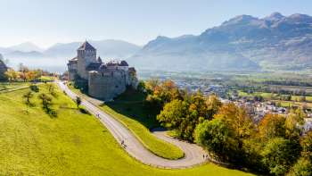 Château de Vaduz sur une colline avec vue sur la vallée du Rhin et les montagnes environnantes.
