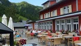 Terrasse ensoleillée du restaurant avec tables couvertes, parasols et vue sur les Alpes.