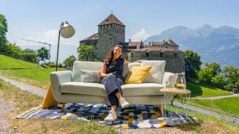 Se détendre avec vue sur le château - un cadre moderne en plein air devant le château de Vaduz Femme assise sur un canapé avec vue sur le château de Vaduz et les montagnes du Liechtenstein, ambiance moderne en plein air avec décoration