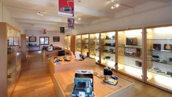 Vue sur une salle d'exposition lumineuse du musée Lawena avec des vitrines éclairées remplies d'appareils électriques historiques.