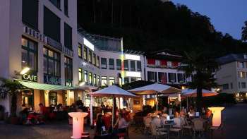 Ambiance de soirée devant la Brasserie Burg à Vaduz avec terrasse illuminée et clients sous parasols. Ambiance de soirée devant la Brasserie Burg à Vaduz avec terrasse illuminée et clients sous parasols.