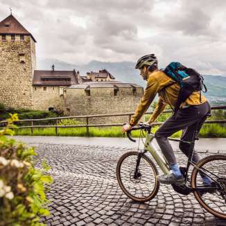 Un gravelbiker roule sur des pavés en direction du château de Vaduz - décor historique et excursion sportive au Liechtenstein