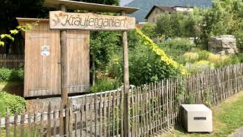 Panneau en bois avec l'inscription "Kräutergarten" (jardin d'herbes aromatiques) à l'entrée du jardin aménagé avec amour à Mauren, entouré de nature et de montagnes.