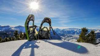 Deux raquettes à neige dans le village enneigé de Malbun, devant une vue panoramique sur les Alpes à l'Alpspitz au Liechtenstein, sous un soleil radieux.