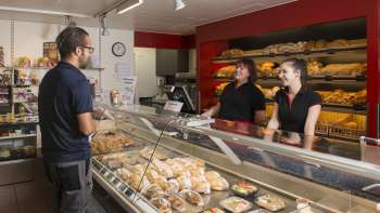 Espace de vente d'une boulangerie avec un personnel aimable, du pain et des gâteaux fraîchement sortis du four au premier plan