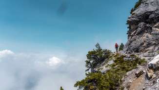 Randonneurs sur l'étroit Fürstensteig (« Chemin des princes ») au Liechtenstein, avec vue sur les nuages en contrebas du sentier.