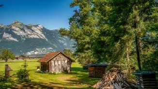 Petite grange en bois sur une prairie avec pile de bois de chauffage et vue sur les Alpes le long de la Route 66 au Liechtenstein