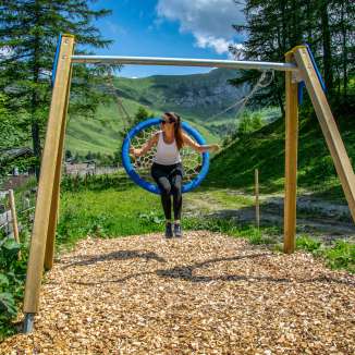 Une femme se balance sur une balançoire à Malbun, au Liechtenstein, entourée de montagnes, de prairies et de nature estivale.
