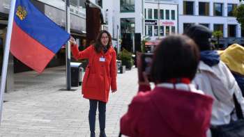 Une guide portant le drapeau du Liechtenstein accueille un groupe de touristes à Vaduz