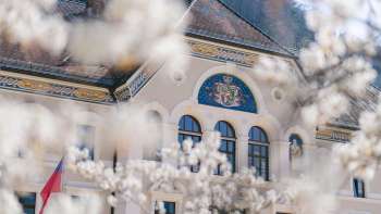 Façade du bâtiment du gouvernement à Vaduz, encadrée d'arbres en fleurs blanches au printemps.