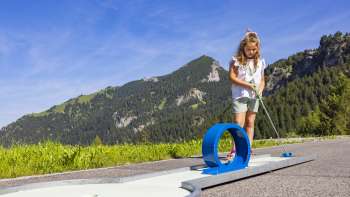 Une jeune fille se concentre sur une piste de looping bleue dans un décor alpin en jouant au mini-golf.