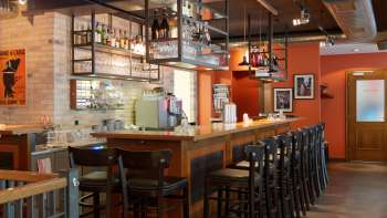 oune bar au New Castle Vaduz avec un long comptoir en bois, des chaises hautes et des étagères en verre suspendues dans une ambiance chaleureuse.