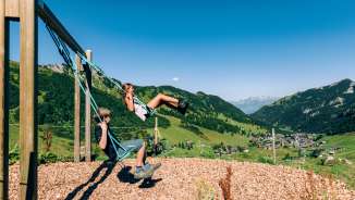 Deux enfants se balancent sur une aire de jeux de montagne avec vue sur le panorama estival de Malbun au Liechtenstein.