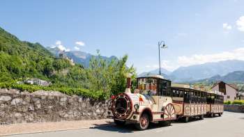 Le train des princes traverse la ville ensoleillée de Vaduz avec une vue sur le château en arrière-plan.