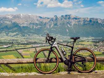 Vélo gravel appuyé contre la clôture ci-dessus Planken avec vue panoramique sur la vallée du Rhin et les Alpes du Liechtenstein – endroit idéal pour les cyclistes
