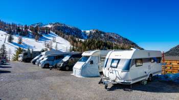 Plusieurs camping-cars sont stationnés sur l'emplacement ensoleillé de Malbun, avec un panorama de montagnes en arrière-plan.