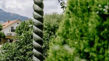 Œuvre d'art Renaissance de Daniel Spoerri avec une forme de colonne marquante et une figure en bronze, entourée de nature au Liechtenstein.