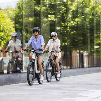 Deux femmes sur des vélos électriques traversent le centre moderne de Vaduz au Liechtenstein, avec sa façade en verre et son ambiance urbaine.