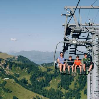 Famille avec enfants sur un télésiège au-dessus des montagnes verdoyantes de Malbun - Aventure estivale et vue panoramique au Liechtenstein