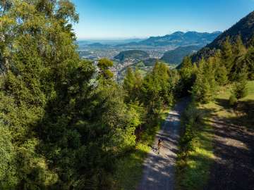 Cyclistes sur un chemin forestier dans les montagnes au-dessus du Liechtenstein avec une vue étendue sur la vallée du Rhin jusqu'aux Alpes suisses.