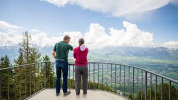 Deux personnes apprécient la vue du point de vue de Gaflei sur la vallée du Rhin au Liechtenstein par temps clair.