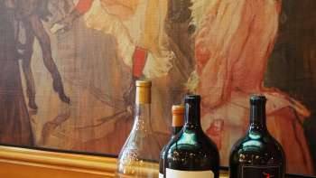 Trois bouteilles de vin devant une fresque artistique à la Brasserie Burg - l'élégance méditerranéenne rencontre le flair artistique.