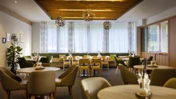 Un autre coin de la salle à manger, avec les mêmes tables rondes, une ambiance chaleureuse et des installations lumineuses modernes.