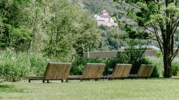 Pelouse calme avec chaises longues en bois dans le parc naturel Haberfeld, avec vue sur le château en arrière-plan.