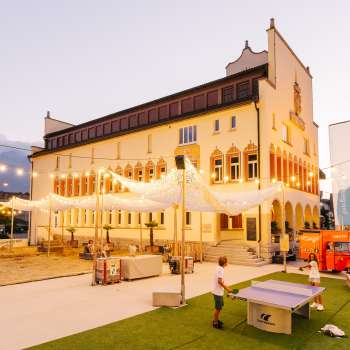 Place de l'hôtel de ville de Vaduz dans une ambiance de soirée lors d'un jour de marché animé avec la foule, les stands de vente et un éclairage d'ambiance.